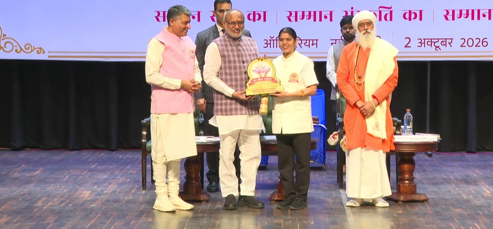 आयुष्य मन्दिरम् की योग प्रमुख योगाचार्य सुषमा को उपराष्ट्रपति द्वारा सम्मान प्रदान किए जाने का दृश्य